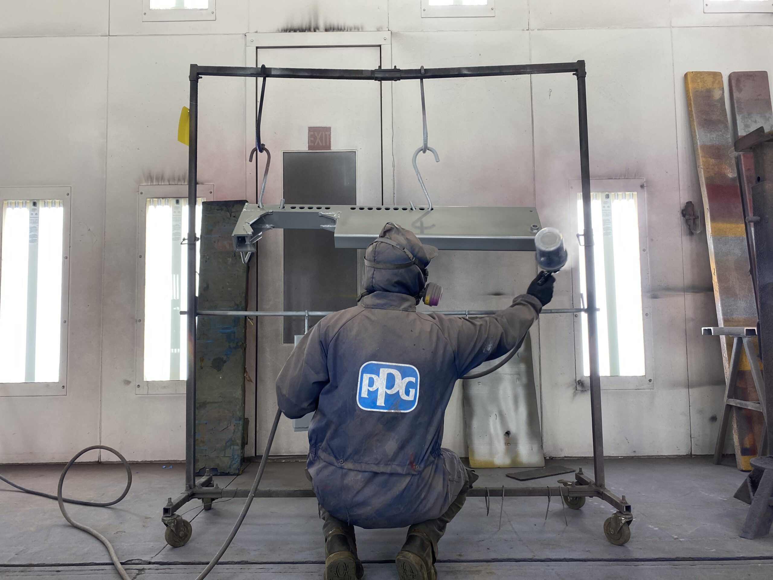 Technician applying industrial coating to drill rig component in paint booth, part of Diedrich Drill’s in-house manufacturing process.