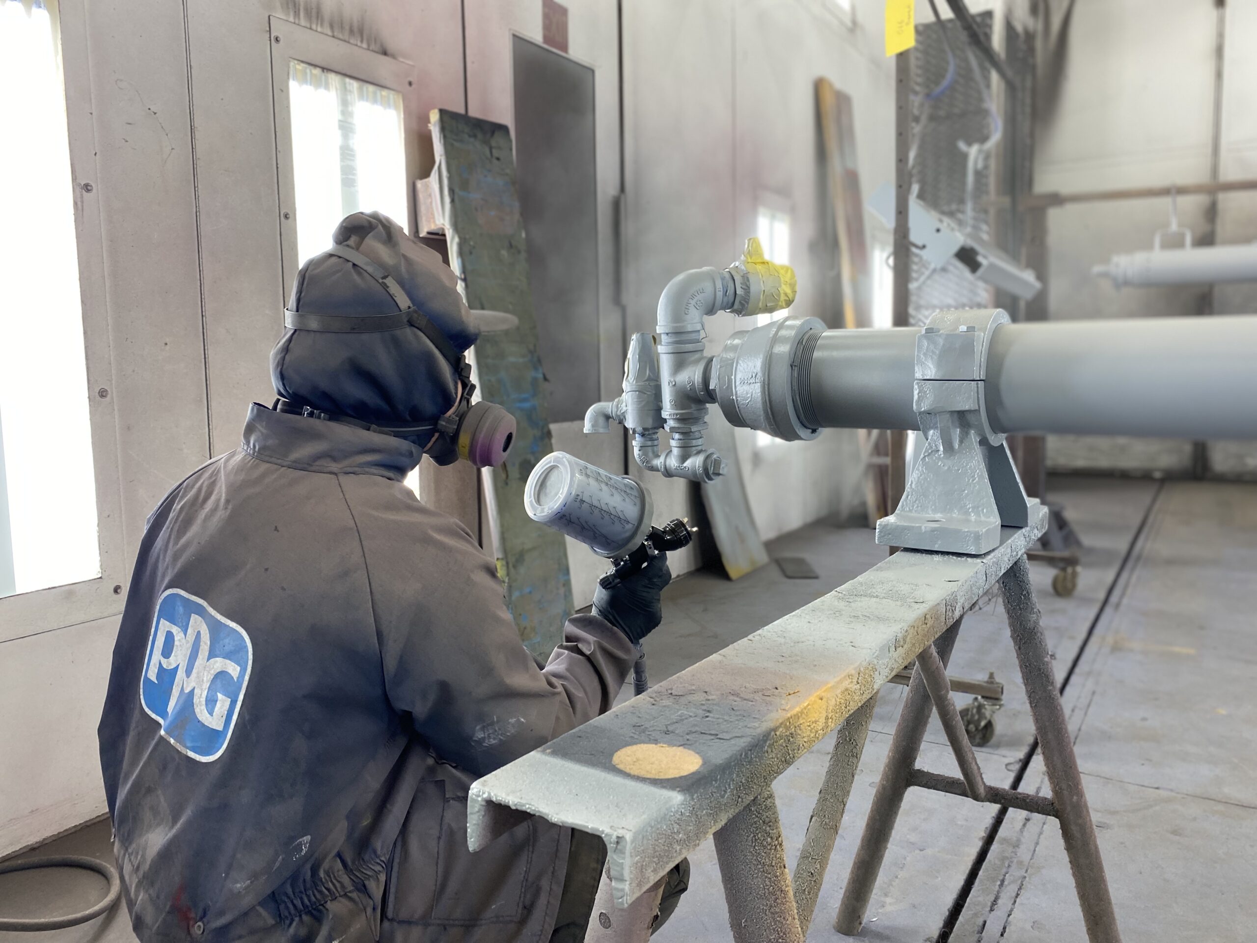 Close-up of technician spray coating drilling equipment components, showcasing Diedrich Drill’s precision manufacturing and finishing process.